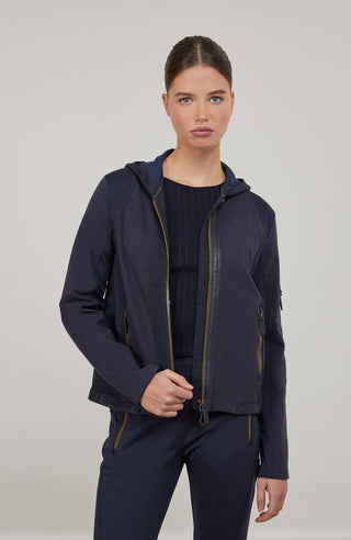 Moderne Damen-Jacke mit Kapuze aus hochwertigem Materialmix aus Baumwolle, Leinen und Elasthan. Die Jacke kombiniert atmungsaktive Baumwollpartien an Vorder- und Rückenteil mit elastischen Natural-Powerstretch-Einsätzen an Kapuze, Ärmeln und Rumpfinnenseite für hohen Tragekomfort und optimale Bewegungsfreiheit. Ausgestattet mit zwei Eingrifftaschen mit Zipp, beidseitig zu öffnendem Frontreißverschluss und edlen, waschbaren Alcantara-Lederdetails. Vielseitig kombinierbar für sportliche, urbane oder casual Lo