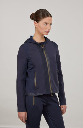 Moderne Damen-Jacke mit Kapuze aus hochwertigem Materialmix aus Baumwolle, Leinen und Elasthan. Die Jacke kombiniert atmungsaktive Baumwollpartien an Vorder- und Rückenteil mit elastischen Natural-Powerstretch-Einsätzen an Kapuze, Ärmeln und Rumpfinnenseite für hohen Tragekomfort und optimale Bewegungsfreiheit. Ausgestattet mit zwei Eingrifftaschen mit Zipp, beidseitig zu öffnendem Frontreißverschluss und edlen, waschbaren Alcantara-Lederdetails. Vielseitig kombinierbar für sportliche, urbane oder casual Lo