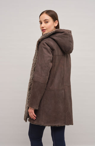 Damen Lammfellmantel mit Kapuze von Frauenschuh, Modell Olivera in der Farbe dunkelbraun Model Rueckansicht– luxuriöser Wintermantel aus hochwertigem Lammfell für stilvolle Wärme.