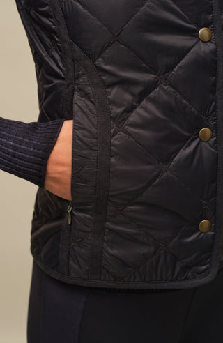 Sportliche Reiterweste Nora Quilt aus leichtem Quilt Light mit 40 g Hochdaunen-Vlies für angenehme Wärme bei minimalem Gewicht. Atmungsaktiv sowie wasser- und schmutzabweisend. Kleiner Stehkragen, mit Leinen eingefasste Nähte und hochwertige Metalldruckknöpfe prägen den klaren Look. Seitliche Taschen mit nahtfeinem Reißverschluss sorgen für Funktionalität. Das fein gesteppte italienische Nylon im klassischen Rautenmuster verleiht der Weste eine elegante, sportive Optik. Leicht verstaubar und ideal für unter
